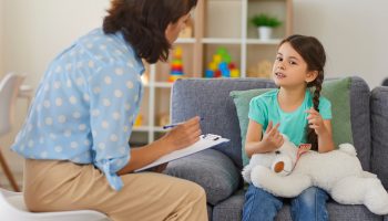 Supportive,Psychologist,With,Clipboard,Listening,To,Little,Child,During,Therapy