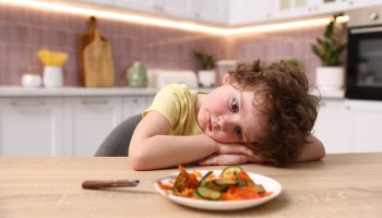 Unhappy,Little,Boy,Refusing,To,Eat,Vegetables,At,Wooden,Table